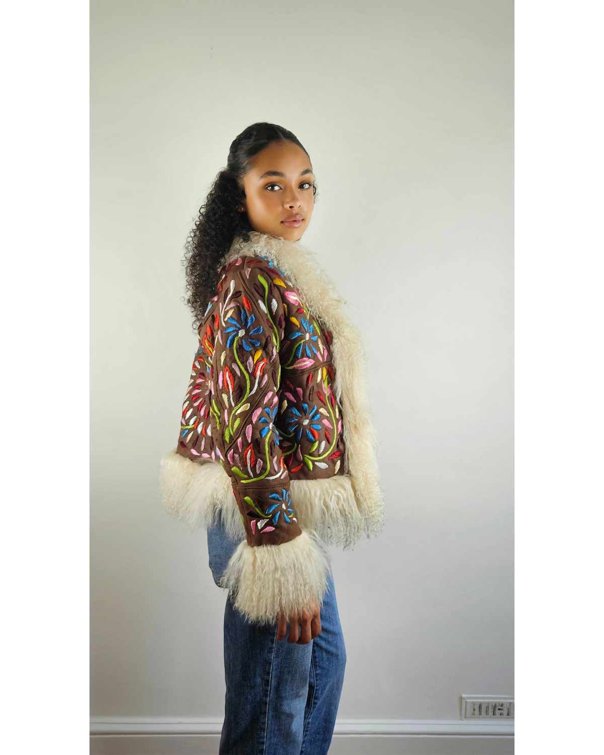 Aql&Nafs Mamuda Jacke aus kupferfarbenem Wildleder mit handgestickten Blumenmustern und weißem Lammfellbesatz.